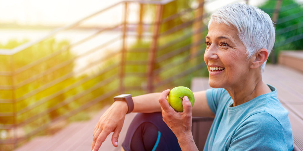 active middle age dental patient eating apple outside with knee up