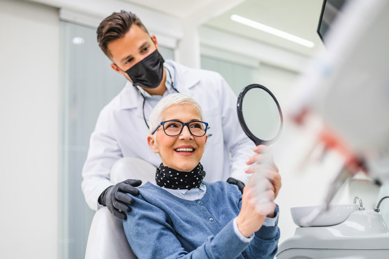 a dental implant patient smiling at her new, affordable smile with her doctor.